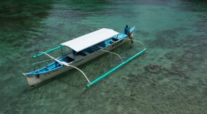 a local from the Philippines is sitting on the bow of a small boat in turquoise green water