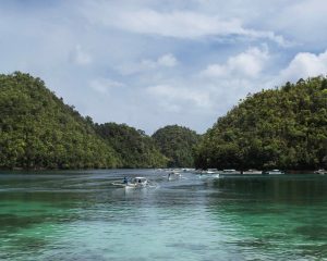 a view of Sugba Lagoon - turquoise water with three boats in the foreground flows into tall mangrove forests that resemble hills.