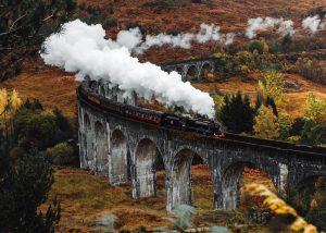 Fall foliage surrounds the Harry Potter Train in the Scottish Highlands, one of the best times to visit Scotland.