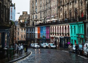 A colorful street lined with shops curves below historic cobblestone buildings in Edinburgh, Scotland.