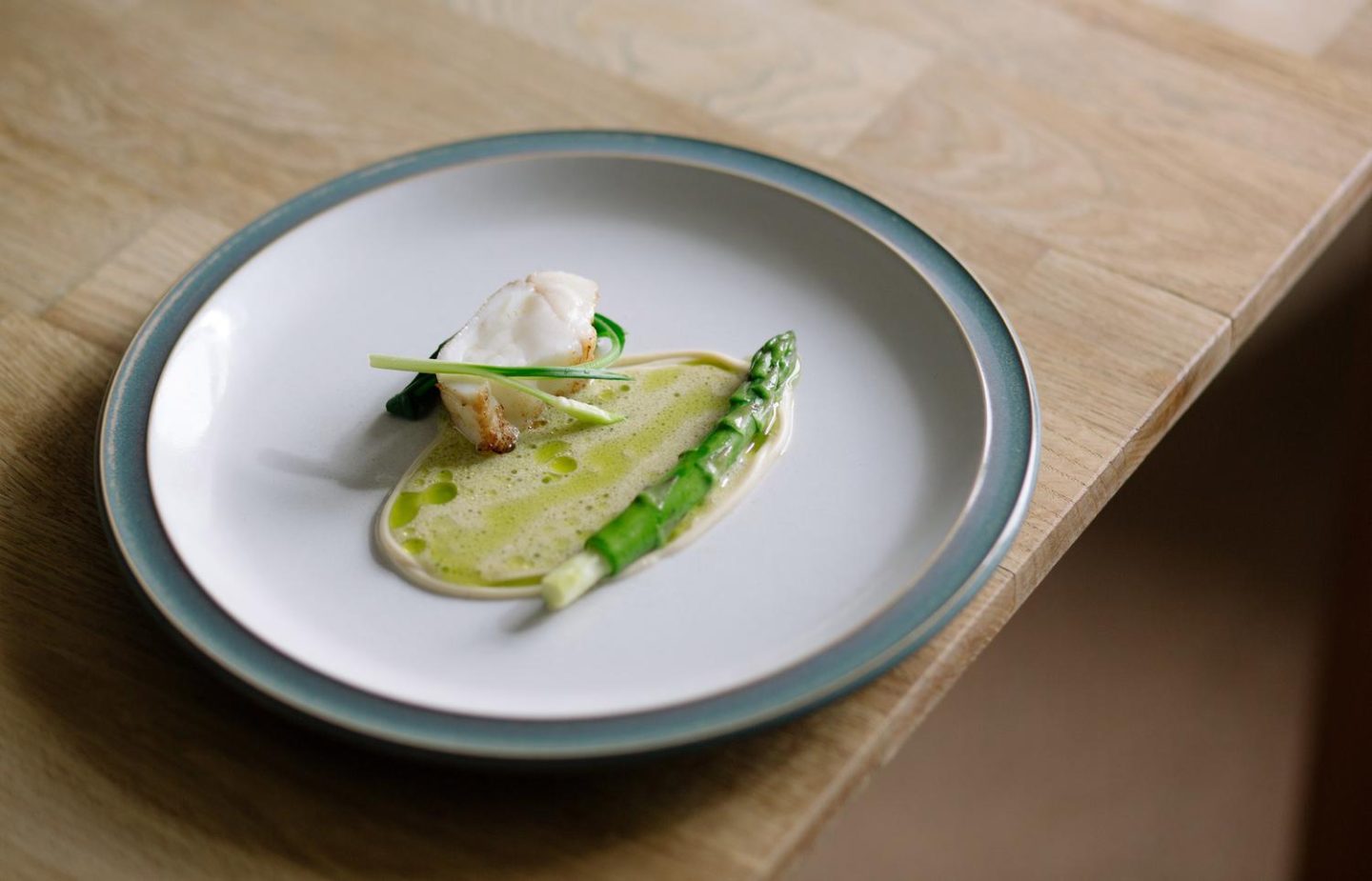 A fine dining dish at Scorrybreac restaurant in Portree on the Isle of Skye, featuring a piece of white fish served with asparagus, a green herb sauce, and delicate garnish on a minimalist plate.