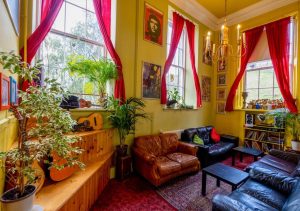 Lively common room at Castle Rock Hostel, Edinburgh. Yellow walls, red curtains, guitars, comfy sofas, and cool posters create a welcoming vibe in one of the best hostels.