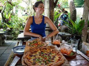 a table with pizza and drinks spreads out in front of a girl smiling at Pizza in the Sky in Northern Okinawa