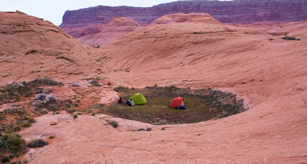 a grass patch surrounded by sandstone at the Reflection Canyon viewpoint with two tents pitched