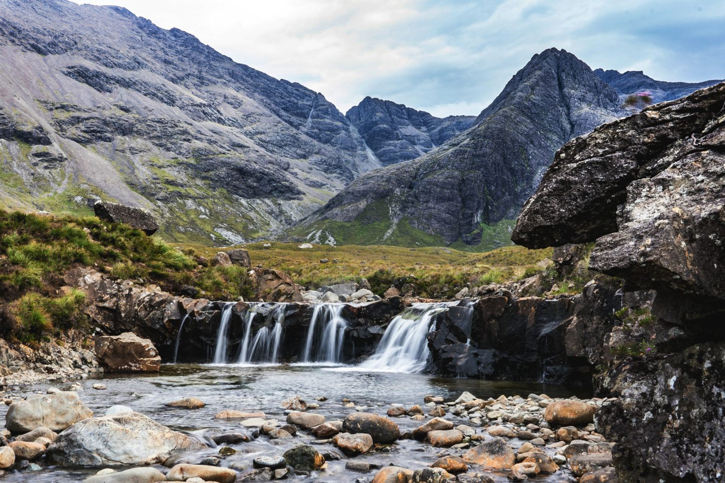 A serene view of the Fairy Pools on the Isle of Skye, where crystal-clear waterfalls cascade over dark rocks beneath the towering Cuillin mountains. This magical stop is a must-visit on any Isle of Skye itinerary, perfect for a scenic hike, a refreshing dip, or simply soaking in the island’s natural beauty.