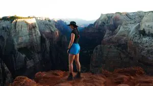 A woman in hiking clothing looking at the camera while standing in front of a scenic canyon vista where granite and red sandstone merge