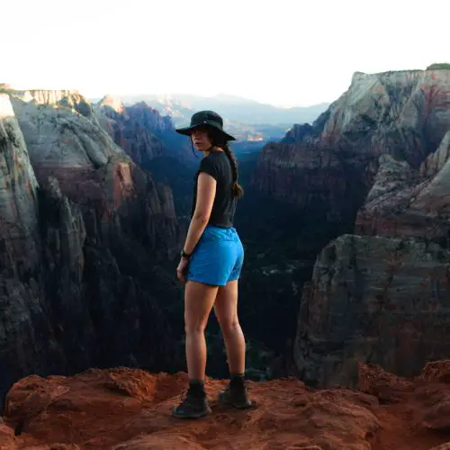 A woman in hiking clothing looking at the camera while standing in front of a scenic canyon vista where granite and red sandstone merge