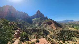 A tall pointed desert rock formation soars above steep and lush terrain along the Watchman Trail, one of the best easy hikes in Zion