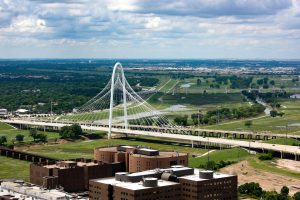 An aerial view of the Margaret Hunt Hill Bridge crossing over the Trinity River. It crosses two neighborhoods that makes visitors wonder, is Dallas safe?