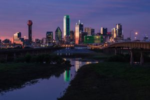 The Trinity River is in the foreground of a nighttime photo of the Dallas skyline. 