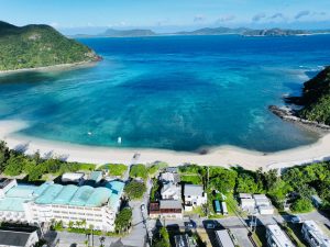 An aerial view of a beachside town hugging vibrant blue Kerama blue water in Okinawa, Japan.