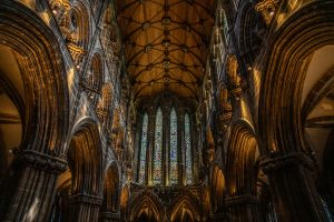 A stunning interior view of a historic church in Glasgow, Scotland, featuring high vaulted ceilings with intricate wooden beams and stained-glass windows. The stone arches and pillars are dramatically lit, emphasizing the building's gothic architecture.
