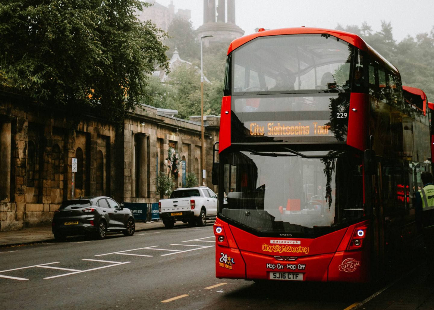 A bright red double-decker City Sightseeing bus in Edinburgh, Scotland, with misty historic buildings in the background—perfect for travelers beginning their Edinburgh to Isle of Skye journey.