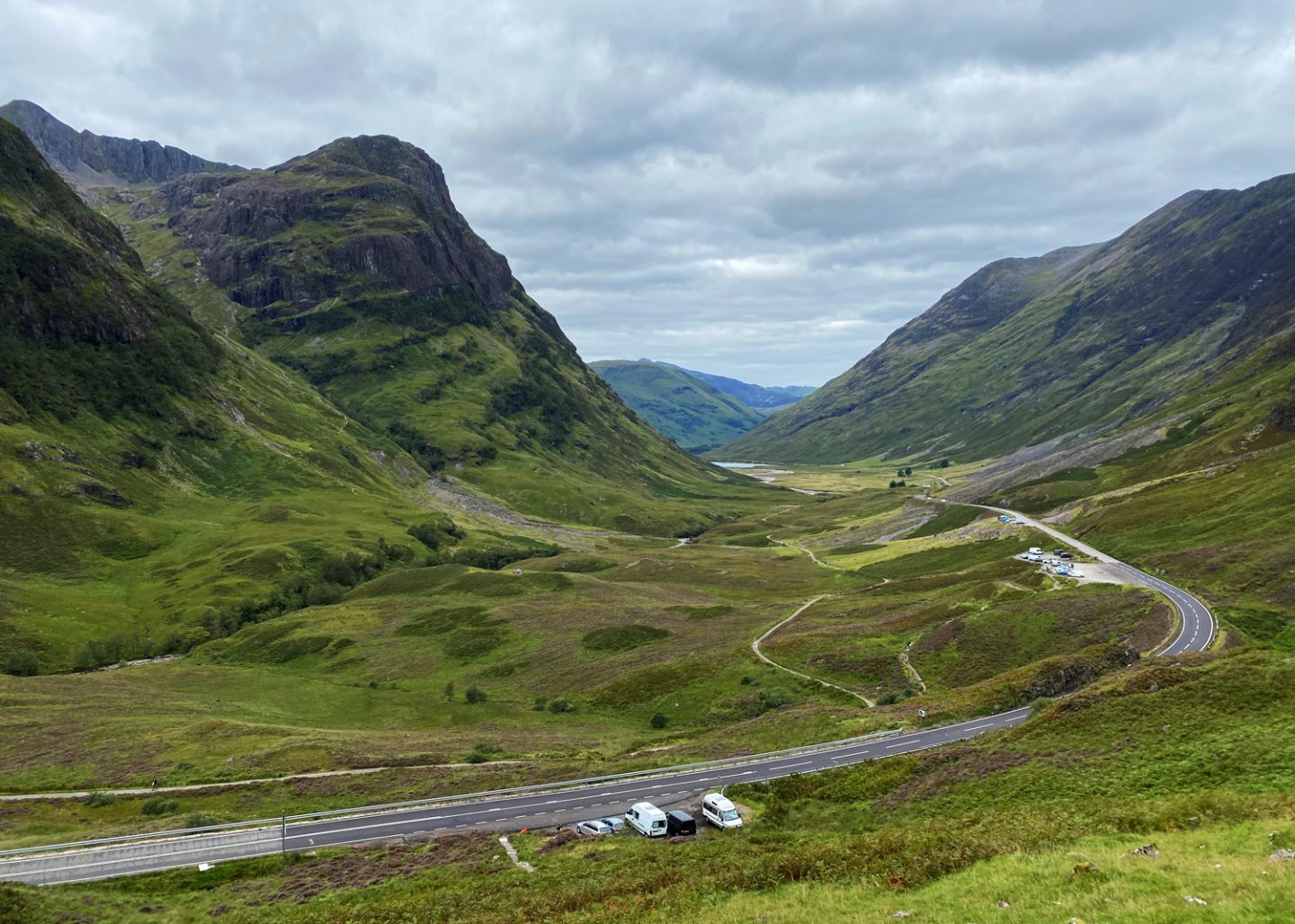Scenic view of the winding road through Glencoe Valley in the Scottish Highlands, surrounded by towering green mountains and dramatic landscapes along the drive from Edinburgh to the Isle of Skye.