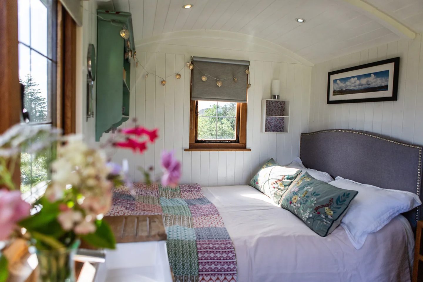 Cozy interior of a Shepherd's Hut accommodation on the Isle of Skye, featuring a comfortable bed, window views of the Scottish landscape, and string lights.