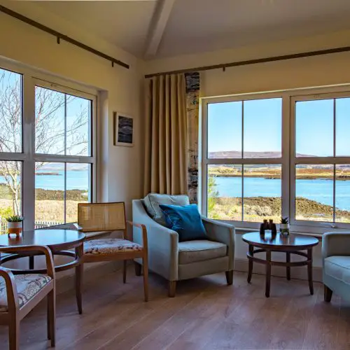 Interior of a luxury suite in The House Over-By accommodation at The Three Chimneys, Isle of Skye, with large windows overlooking the beautiful coastal loch and shoreline.